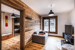 Uma sala de estar moderna com uma parede de destaque em madeira, um sofá cinza, um rack para televisão e uma janela grande com vista para a cidade.