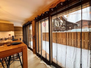 A wooden dining table with chairs, a kitchen area with wooden cabinets, and a view through large windows to a snowy outdoor area. - Wifi, 250m from resort center, Ground floor, terrace, tv, ski locker, 40m², Les Gets (Les Gets)