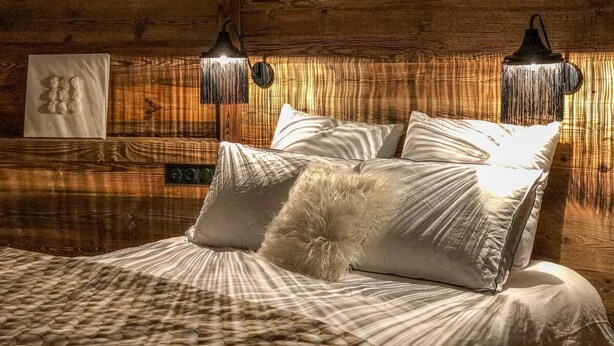 Ein gemütliches Schlafzimmer mit einem Holz-Kopfteil, einem Bett mit weißen Leinen und weichen Kissen sowie zwei Wandlampen.