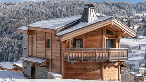 Eine Holzhütte mit Balkon vor einer verschneiten Berglandschaft.