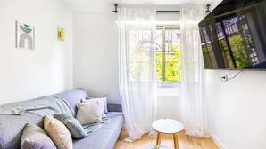A modern living room with a grey sofa, a small round table, and a TV mounted on the wall. - Lavie Maison: Studio Équipé (Bordeaux)