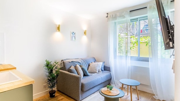 A modern living room with a grey sofa, a small round table, and a potted plant. - Lavie Maison: Studio Équipé (Bordeaux)