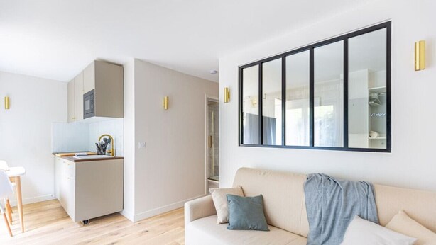 A modern living room with a beige sofa, a small kitchen area, and a large mirror on the wall. - Lavie Maison Cozy Balneo Sauna (Bordeaux)