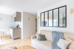 Una sala de estar moderna con un sofá color beige, una pequeña área de cocina y un espejo grande en la pared.