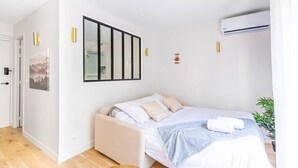 A bedroom with a bed, a bedside table, a wall-mounted air conditioner, and a door. - Lavie Maison Cozy Balneo Sauna (Bordeaux)