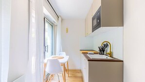 A compact kitchen with a wooden countertop, a sink with a gold faucet, and a microwave above it. There is a dining area with a white table and chairs, and a window providing natural light. - Lavie Maison Cozy Balneo Sauna (Bordeaux)