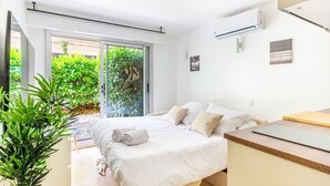 A modern bedroom with a bed, a wooden desk, and a sliding glass door leading to a balcony with greenery.