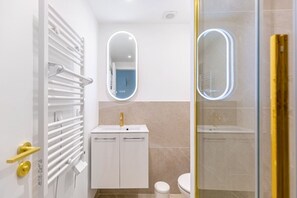 Ein modernes Badezimmer mit einem weißen Waschtisch, einem goldenen Wasserhahn und einer Glasdusche.