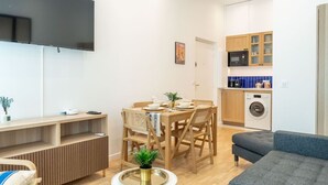 A modern living room with a flat-screen TV, wooden dining table, and grey sofa. - Lavie Maison A/C & Balneo (Paris)