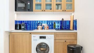 Une cuisine compacte équipée d’un four à micro-ondes Bosch, d’un lave-linge Miele et de meubles de rangement en bois.