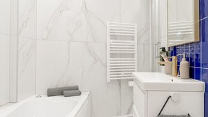 A modern bathroom with a white bathtub, a white toilet, and a towel rack. - Lavie Maison A/C & Balneo (Paris)