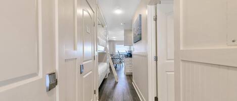 A narrow hallway with white doors, a bunk bed, and a kitchen area in the distance.