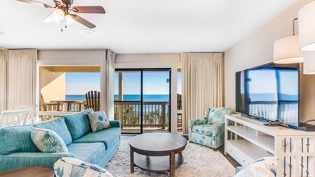 Een moderne woonkamer met een bank, salontafel en tv, met uitzicht op een balkon en de oceaan.