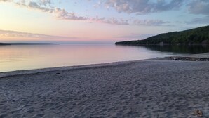 A beach with a calm sea, a sandy shore, and a forested hill in the background.