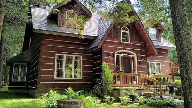 A rustic log cabin with a wooden deck and a stone pathway leading to the entrance.