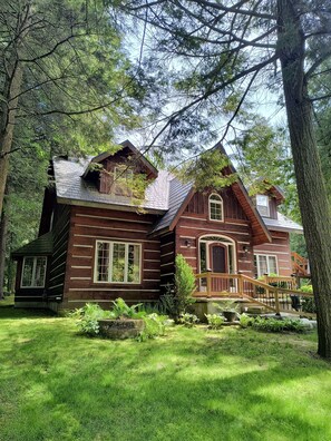 Un chalet rustique en rondins de bois, doté d’une terrasse en bois et d’un chemin de pierre menant à l’entrée.
