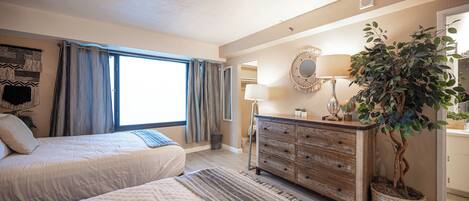Une chambre à coucher avec un lit, une commode, un miroir, une lampe et une plante en pot.
