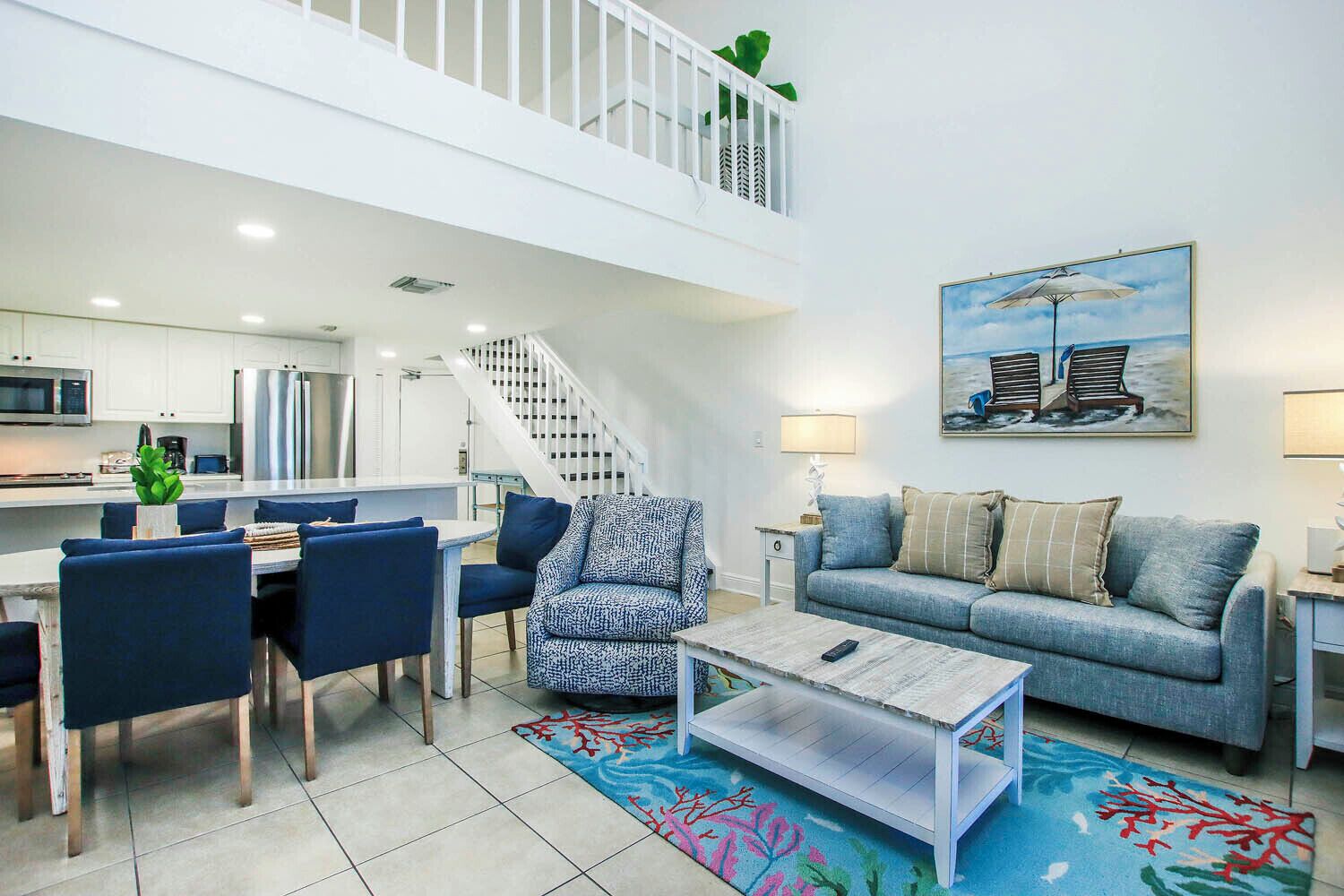 A modern living room with a dining area, a staircase, and a kitchen.