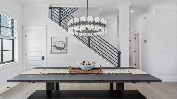 Uma área de jantar moderna com uma mesa de madeira escura, um candeeiro decorativo e uma escadaria com grades pretas.