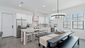 Una cocina moderna con armarios blancos, un refrigerador de acero inoxidable, una isla central con taburetes y una lámpara colgante.