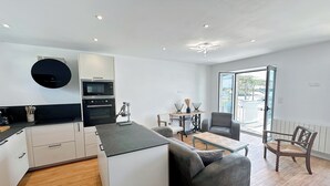 Eine moderne Küche mit weißen Schränken, einer schwarzen Arbeitsplatte und einem eingebauten Backofen. Es gibt einen Essbereich mit Tisch und Stühlen sowie ein großes Fenster mit Blick ins Freie.