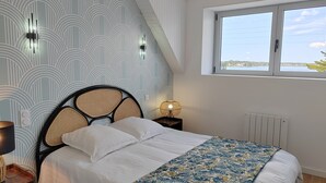 Ein Schlafzimmer mit Bett, Nachttisch, Lampe, Fenster mit Blick und einer Wand mit Muster.
