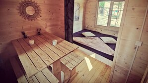 A wooden cabin with a dining table, a bed with a view, and a sun dial on the wall. - 2 Bedroom Chalet in Pruniers-en-Sologne (Pruniers-en-Sologne)