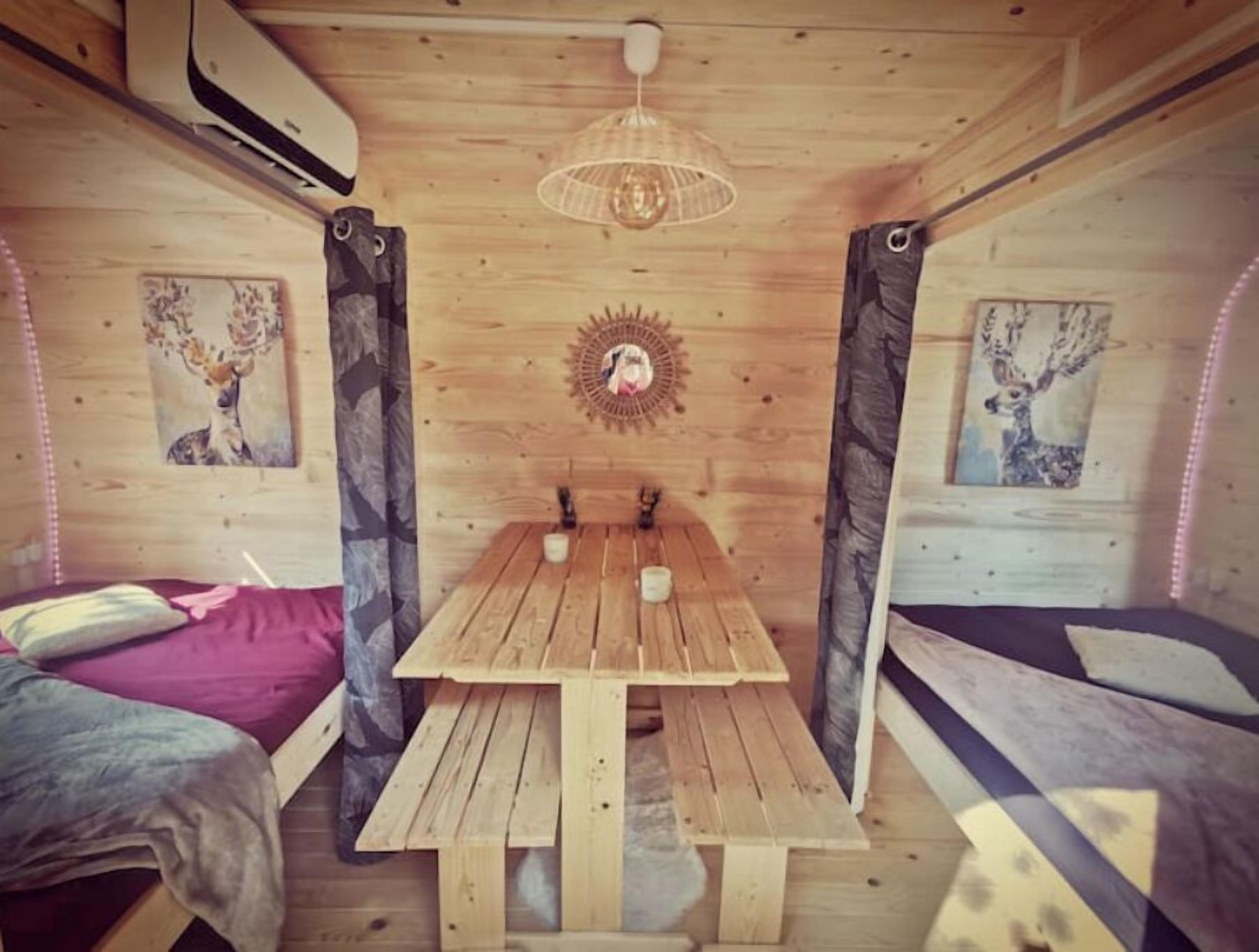 Ein gemütliches Blockhauskabinenzimmer mit Holztisch, zwei Betten und einer Deckenleuchte.