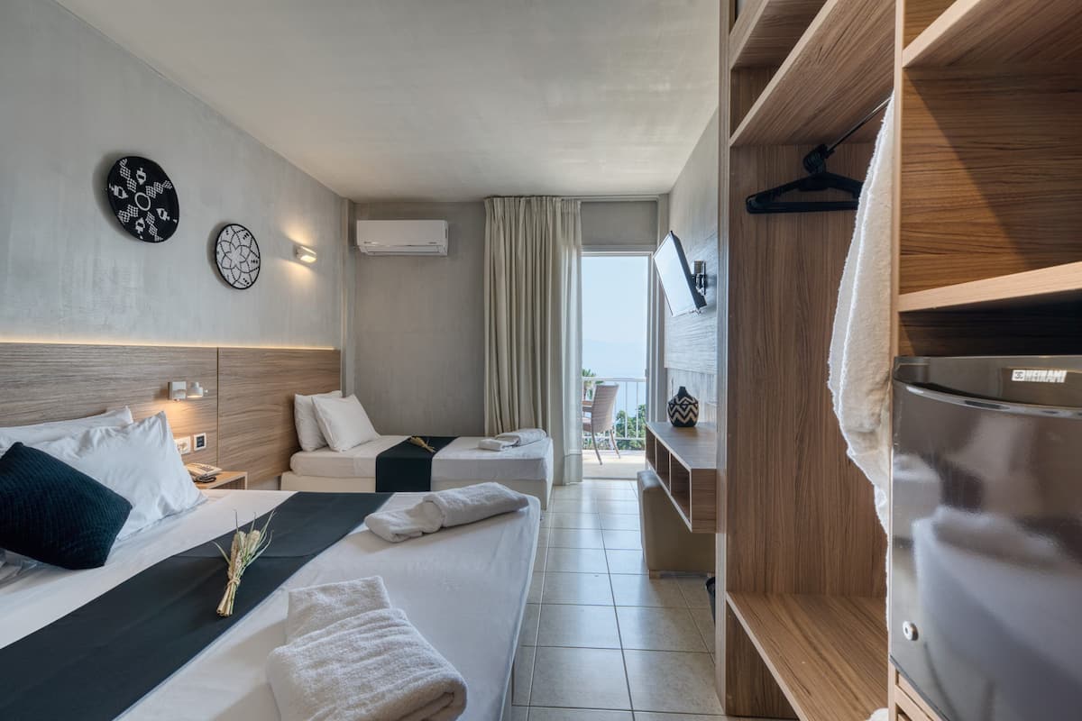 Ein Hotelzimmer mit zwei Betten, einem Schrank, einem Balkon und Meerblick.