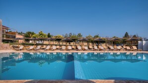 Una piscina con sillas de descanso y sombrillas, rodeada de árboles y edificios.