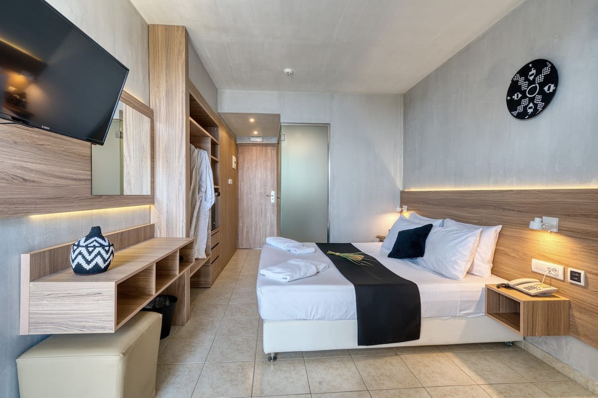Ein modernes Hotelzimmer mit Bett, Nachttisch, Fernseher, Kleiderschrank und Wanduhr.