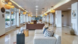 Un vestíbulo amplio con diseño moderno, que cuenta con una zona de estar central con sofás y sillones, un mostrador de recepción alargado e iluminación decorativa.