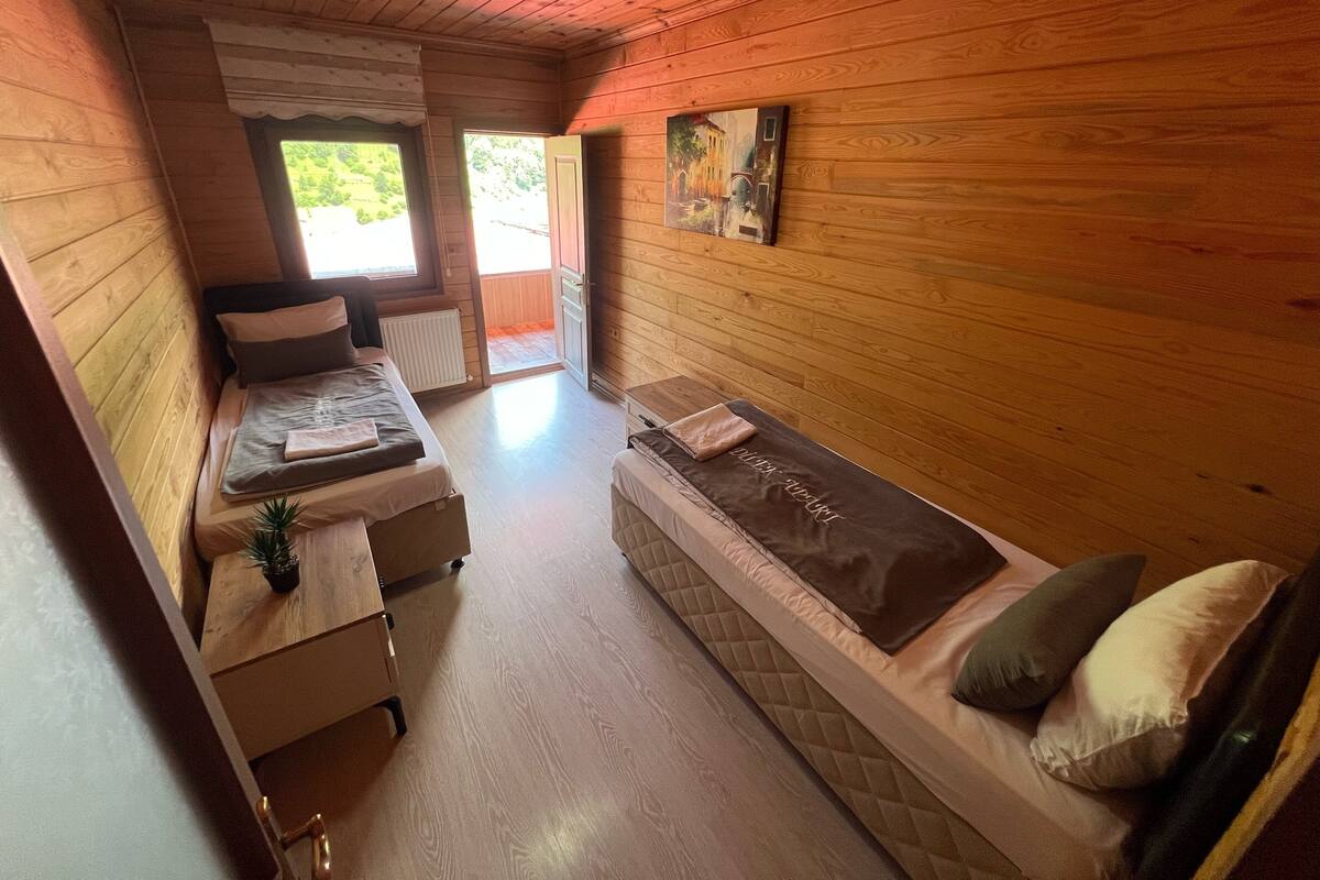 A cozy wooden cabin room with a bed, a bench, and a small table with a plant.