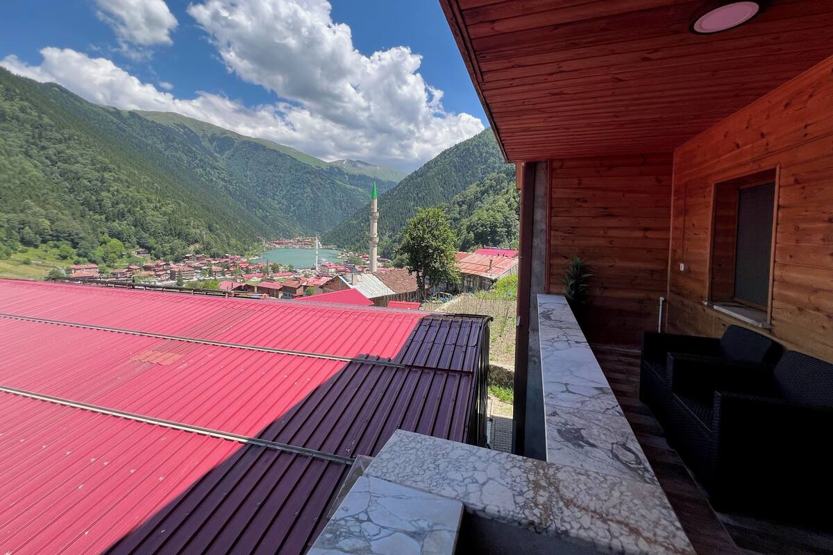 A wooden cabin with a balcony overlooking a village and mountains.
