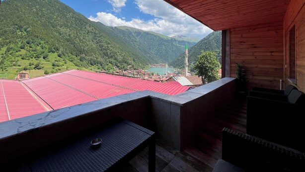 A wooden balcony with a view of a mountainous landscape and a distant town. - DİLEK APART (Çaykara)
