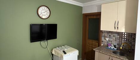 Una cocina compacta con televisor de pantalla plana, un refrigerador pequeño y un lavamanos.
