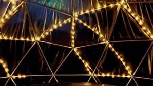 Una estructura en forma de cúpula geodésica con una plataforma circular en la base, iluminada con luces de cadena.