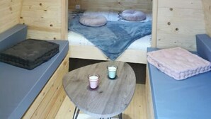 Un acogedor dormitorio en el ático con techo inclinado, una ventana pequeña, cama con almohadas, una mesa con velas y asientos empotrados.