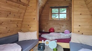 Una cabaña de madera acogedora con una cama en el altillo, dos sofás, una mesita y un ventanal con vistas al exterior.