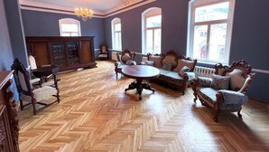 A spacious room with a herringbone wooden floor, ornate furniture, and large windows allowing natural light. - 90qm Luxus Apartment im Schloss Cotta (Dohma)