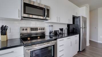 A modern kitchen with white cabinets, stainless steel appliances, a black countertop, and a wooden floor.