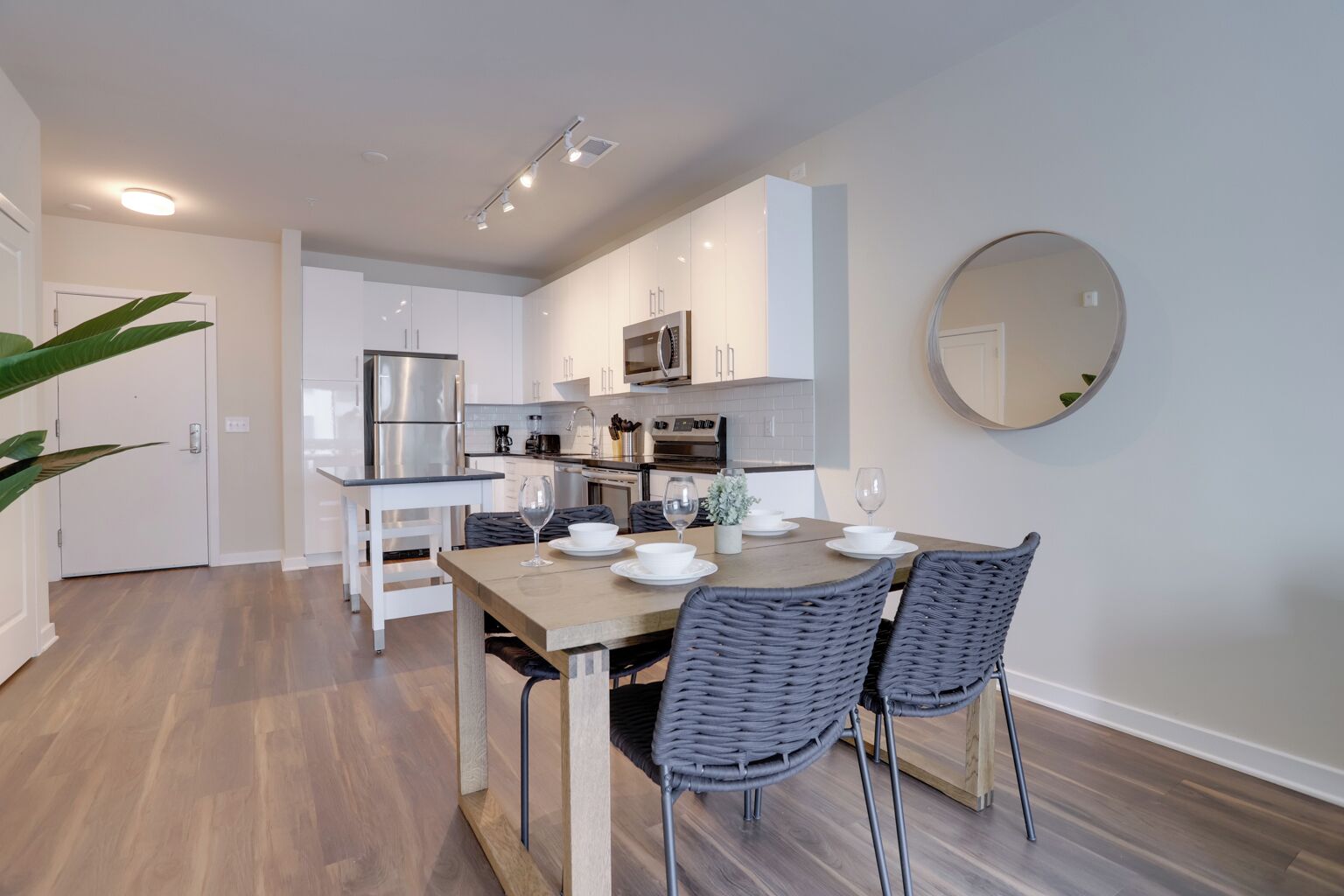 A modern kitchen with white cabinets, a stainless steel refrigerator, and a dining area with a wooden table and wicker chairs.