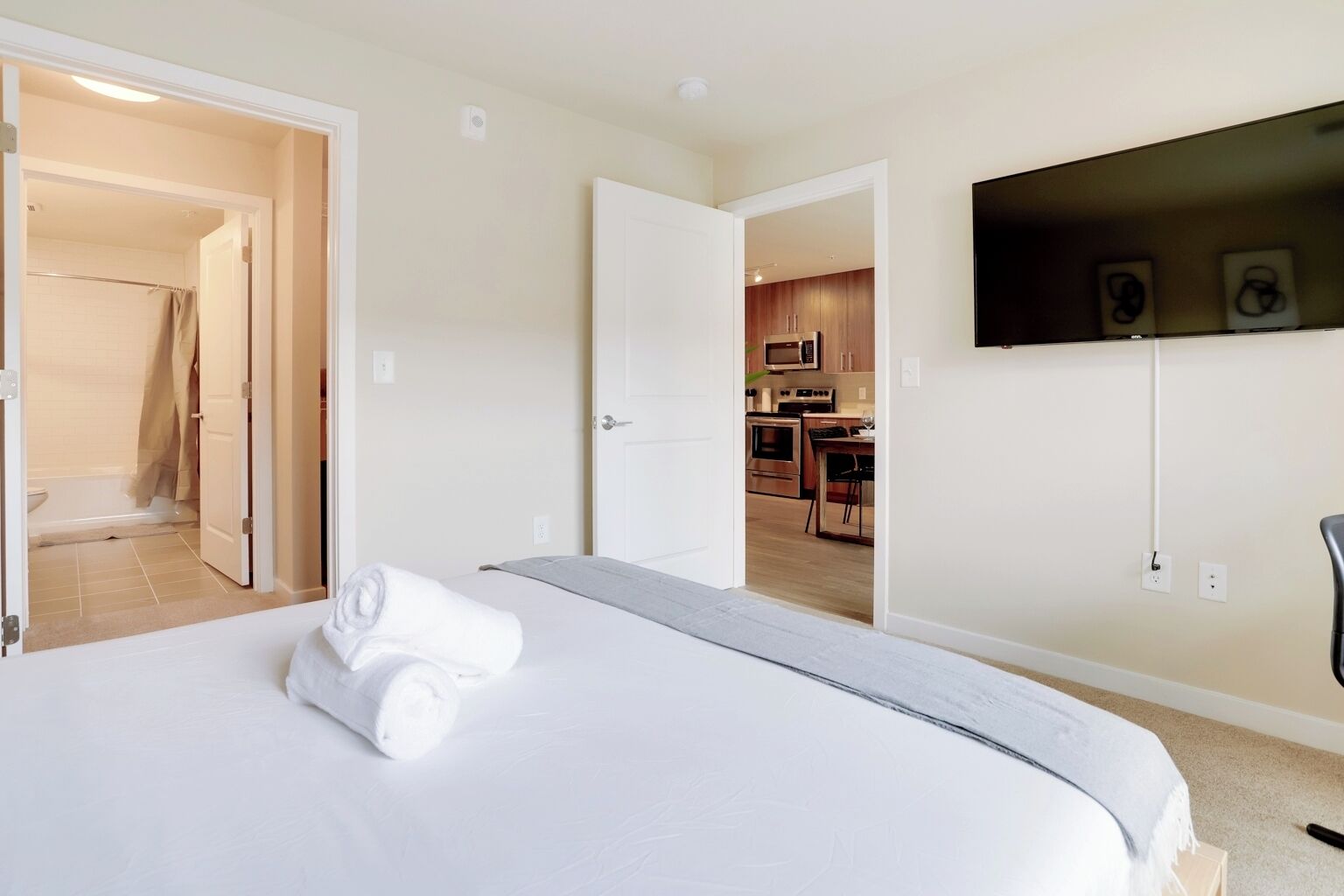Ein Hotelzimmer mit Bett, einem an der Wand montierten Fernseher und Blick in den Küchenbereich.
