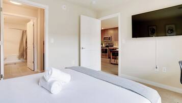 Ein Hotelzimmer mit Bett, einem an der Wand montierten Fernseher und Blick in den Küchenbereich.