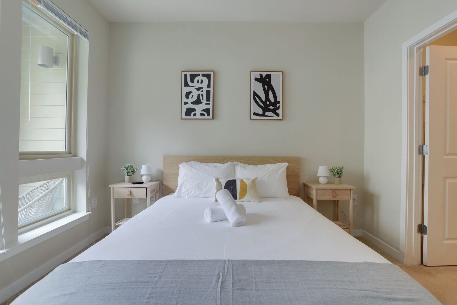 A neatly made bed with white linens, two bedside tables with lamps, and two abstract art pieces on the wall.