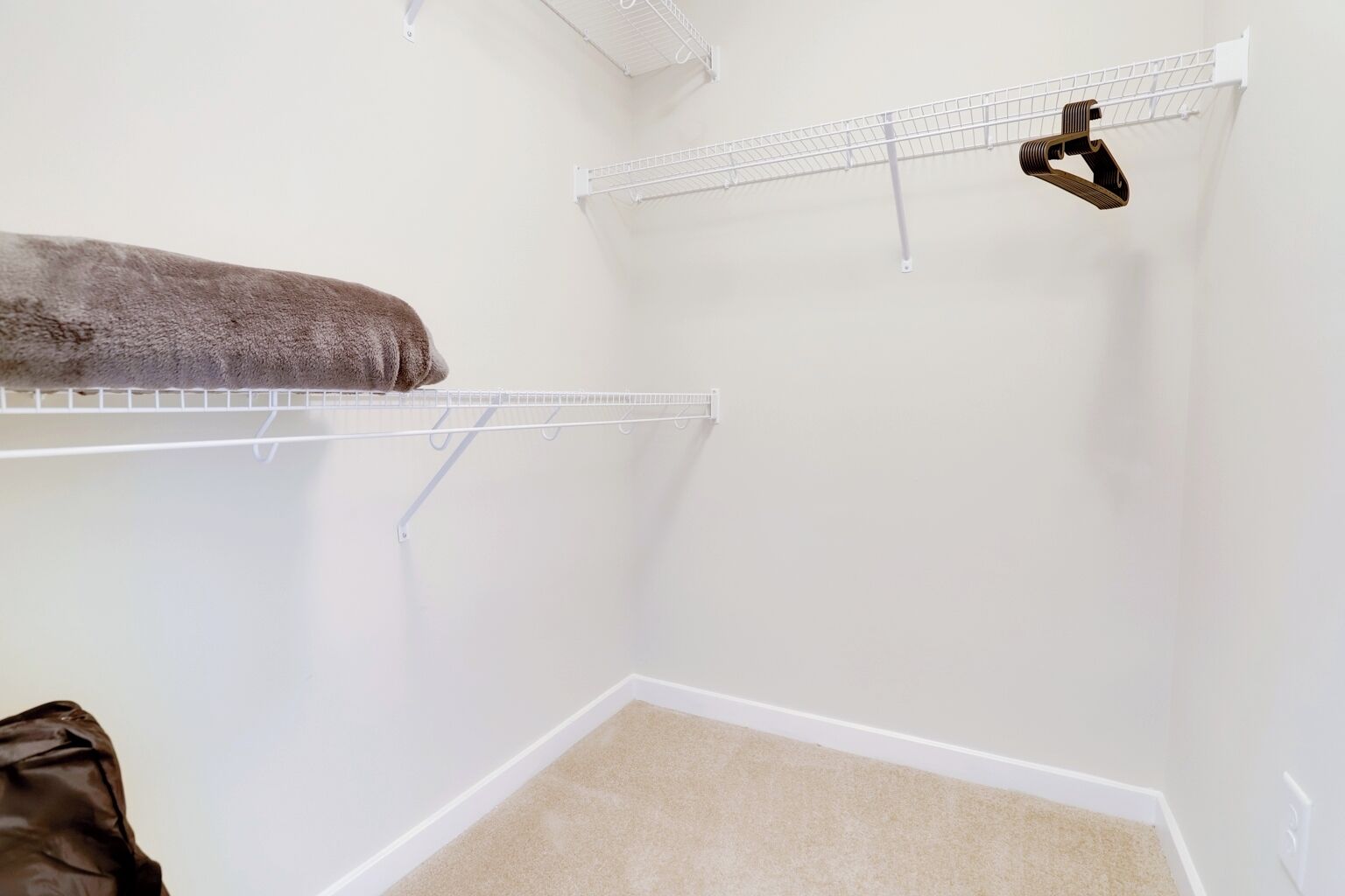 A small, empty room with white walls, a beige carpet, and two white wire shelves.