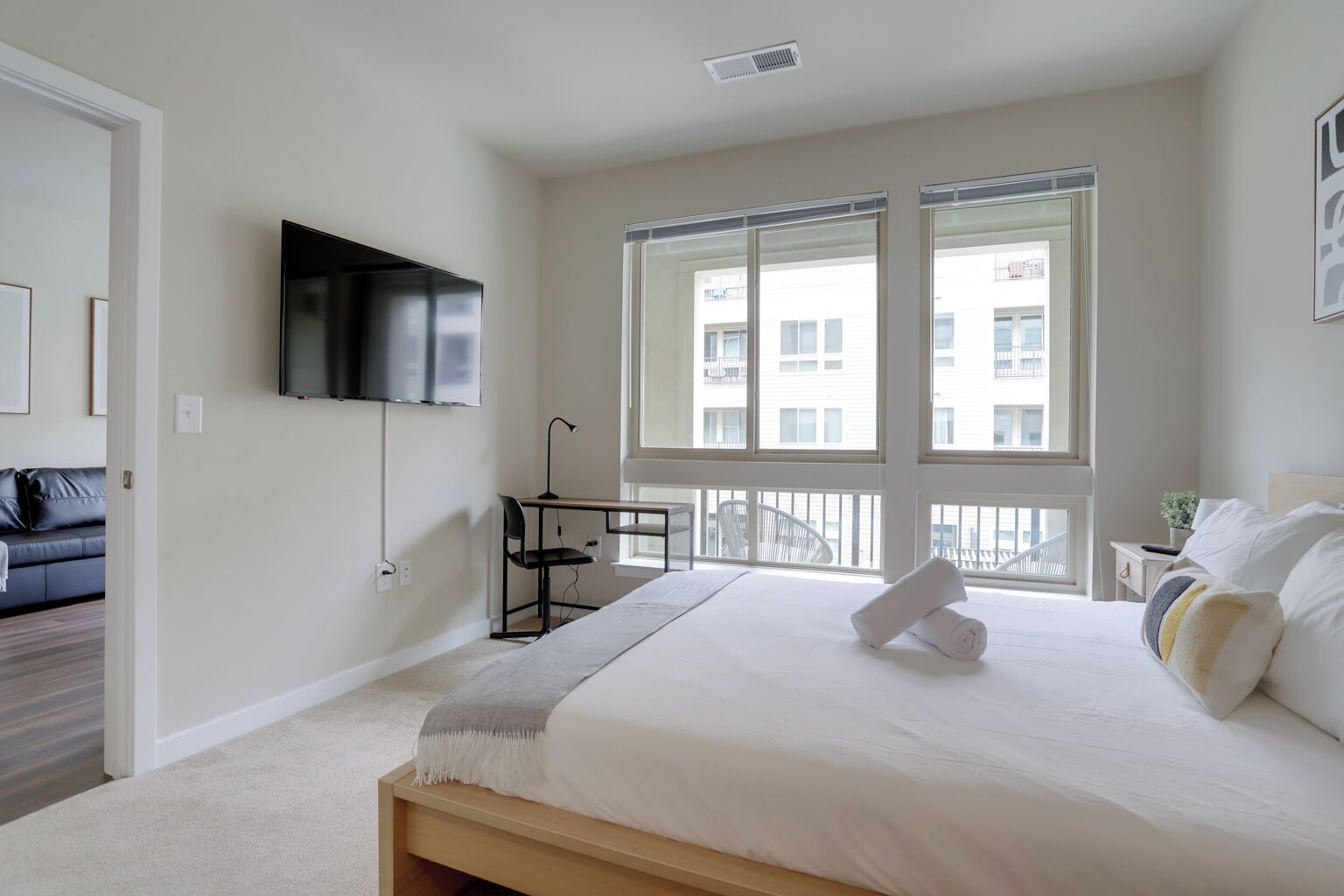 Un dormitorio moderno con una cama grande, un escritorio, una silla, un televisor y ventanas amplias.