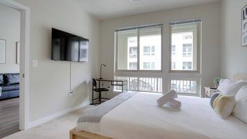 Un dormitorio moderno con una cama grande, un escritorio, una silla, un televisor y ventanas amplias.