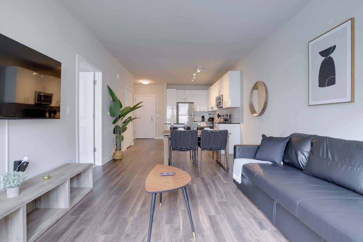 A modern living room with a grey sofa, a small wooden table, and a TV mounted on the wall.