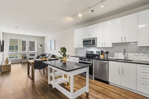 A modern kitchen with white cabinetry, a stainless steel microwave, and a black countertop. - Huntington Apartments near Fort Hunt - We Host (Alexandria)